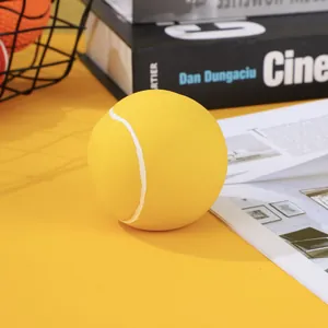 Close-up of a yellow latex dog toy ball with tennis pattern on a yellow desk.