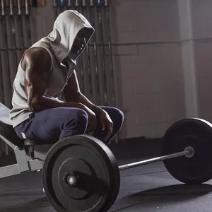 Detailed view of grey sleeveless quick-dry sports gym vest hoodie on muscular man in gym