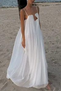 Flowy white spaghetti strap backless maxi dress with metal neck detail on a beach sunset