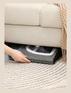 A macro view showing the foldable grey pet house being stored easily under a beige sofa