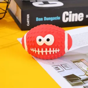 Red squeaky latex rugby ball pet toy with funny cartoon face shown on a magazine