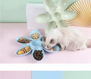 Witte kat die eet uit een blauwe bloemvormige voerbak met meerdere vakken op roze vloer