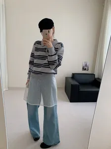 Vue en pied d'une femme portant un pull à rayures grises avec col polo dans un décor épuré.