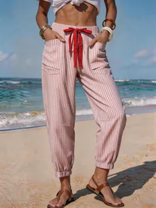 Detail of striped linen-like joggers with red drawstring on a sunny beach background