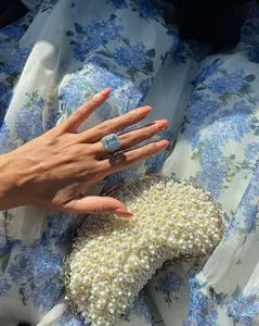 Close-up detail of blue floral organza fabric texture with elegant pearl bag and ring.
