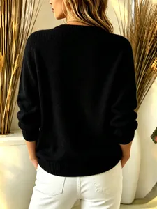 Back view of a women's solid black long-sleeve knit sweater on a model in a warm studio