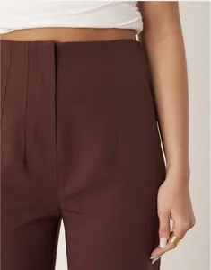 Close-up view of deep brown high-waisted tailored trousers featuring pleated front details
