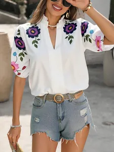 Close-up detail of white V-neck blouse with vibrant floral embroidery on puff sleeves