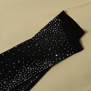Primo piano dettagliato degli strass argentati brillanti su body in rete trasparente nera.