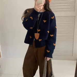 Dettaglio del cardigan in maglia blu con motivi a cuore arancioni e chiusura a zip