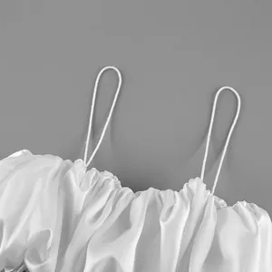 Close-up of a white satin camisole top showing the thin straps and elegant gathered pleated texture
