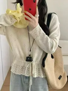 Macro detail showing the beige hollow-out knit cardigan with a unique waist-tie design.