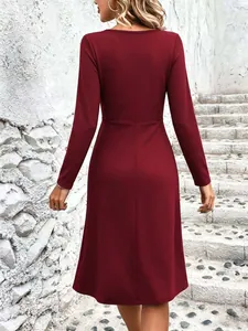 Rear view of burgundy long sleeve midi dress with fitted waist against stone wall