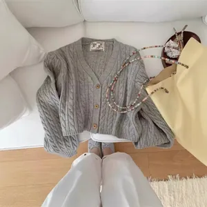 Grey cable-knit short cardigan with wooden buttons in a cozy lifestyle setting