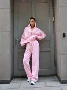Lifestyle shot of a woman wearing a pink hooded tracksuit set in front of a grey door
