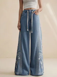 Detailed view of white floral embroidery on high-waisted bohemian wide-leg blue denim jeans