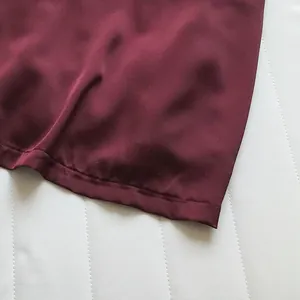 Dettaglio ravvicinato dell'orlo in tessuto raso bordeaux liscio di un top da donna.