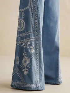 Detailed view of intricate white floral embroidery on blue wide-leg bohemian denim jeans