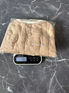 Detailed view of plush tan pet winter coat being weighed on a scale showing 76.2 grams