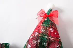 Detail view of red and green plaid pet Christmas cloak with snowflake patterns and red bow