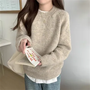 Détail d'un pull en maille crème douce avec un livre et un collier dans un décor très cosy