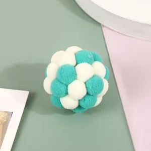 Close-up of a teal and white plush pompom ball toy for cats on a pastel background