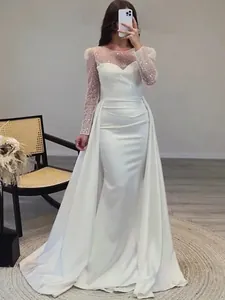 Detailed view of an elegant white sequined long-sleeved evening gown with a flowing train