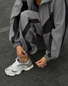 Woman in relaxed grey and black color-block tracksuit tying shoelaces on stone street