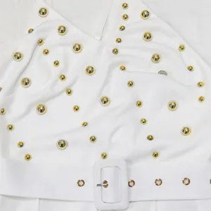 Close-up of white fashion jumpsuit with gold stud embellishments and matching belt