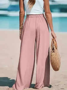 Back view of stylish pink high-waisted wide-leg trousers on a sunny beach setting.