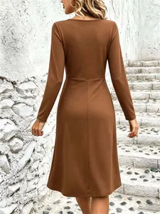 Back view detail of brown V-neck long sleeve midi dress on a textured stone wall