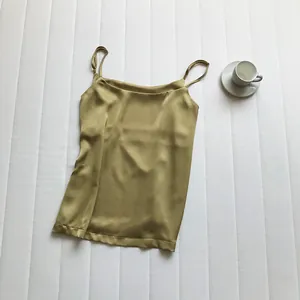 Elegante canotta in raso oro oliva con spalline sottili su sfondo bianco strutturato