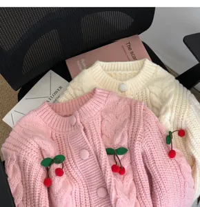 Close-up of pink and cream chunky knit cardigans with 3D cherry decorations
