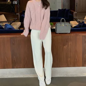 Detailed view of pink cable knit sweater and white wide-leg pants in lounge setting.