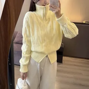 Detail view of pale yellow cable-knit cardigan featuring a double zipper and high collar