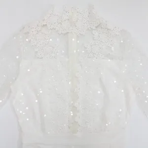 Primer plano de top de encaje blanco con lentejuelas brillantes y cuello alto