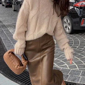 Detailed view of a beige chunky cable-knit sweater paired with a stylish brown leather skirt.