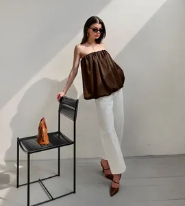 Détail mode d'un haut bandeau en satin marron avec un pantalon blanc à jambes larges.