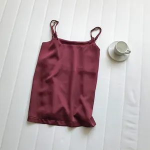 Elegante canotta in raso bordeaux con spalline sottili su sfondo bianco strutturato