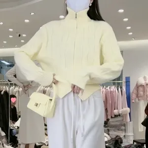 Detail view of cream cable-knit zip-up cardigan on model in clothing store setting