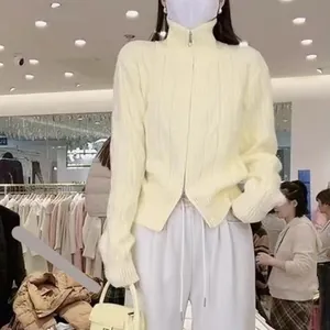 A detailed macro view of the cream cable-knit cardigan featuring a unique double-zipper