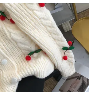 Close-up of cream cable-knit cardigan with cherry decorations and white buttons.