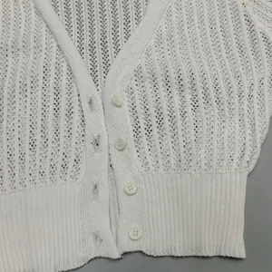 Close-up of white hollow-out knit cardigan with front buttons and ribbed hem detail.