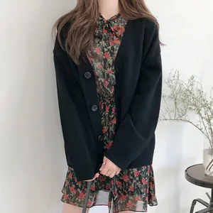Close-up of a minimalist black knitted cardigan layered over a floral rose pattern dress.