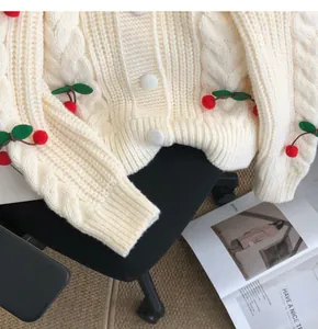 Detail view of cream cable knit cardigan with 3D cherry appliques and soft texture.