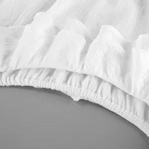 Vue détaillée d'un haut blanc à épaules dénudées avec des volants et une taille élastique.