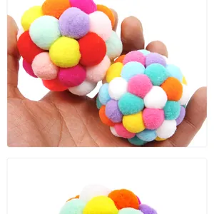 Close-up of colorful plush pom-pom ball cat toy held in hand showing soft texture.