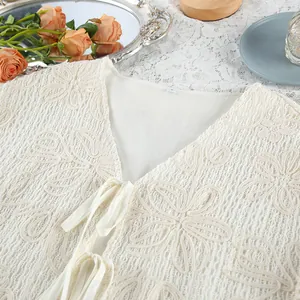 Dettaglio del cardigan in pizzo jacquard crema con lacci anteriori per le vacanze
