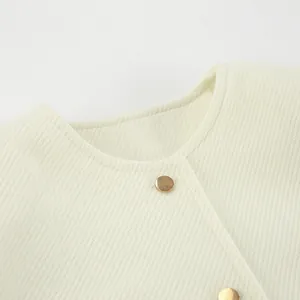 Nahaufnahme des Ausschnitts einer weißen Tweedjacke mit Wollstruktur und Goldknopf