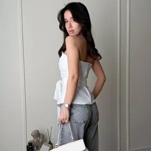 Modell trägt weißes schulterfreies Schößchen-Top mit Taillenband und grauer Jeans